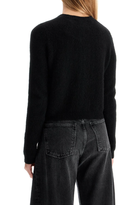 Back view of a person wearing a black long-sleeve knit sweater and dark gray jeans against a plain white background.