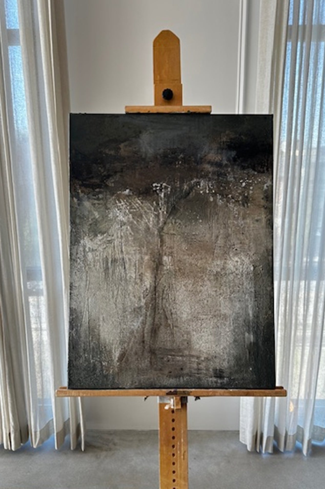 Abstract painting on an easel in a room with curtains