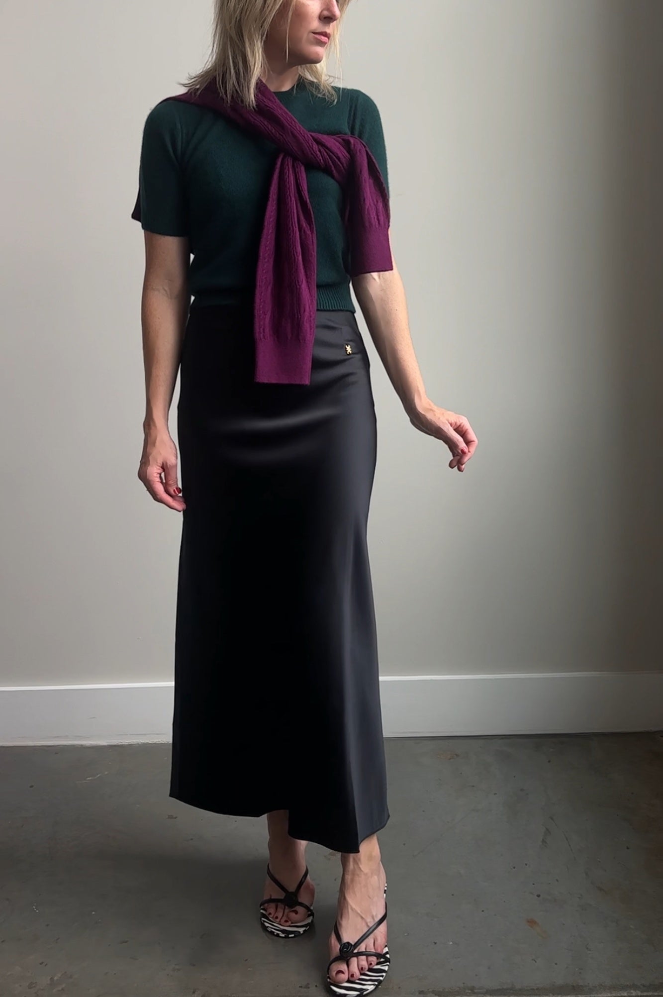 Woman wearing a dark green top, black skirt, and purple scarf against a plain background