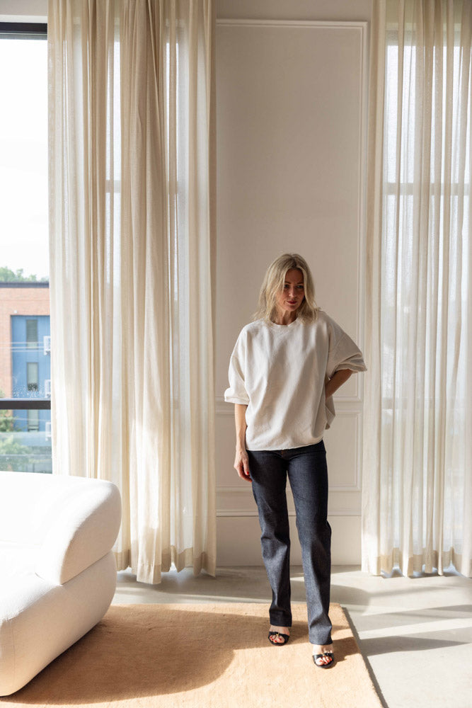 Dagmar Straight Leg Denim in raw blue organic cotton, worn full length with an off-white sweatshirt in a sunlit room