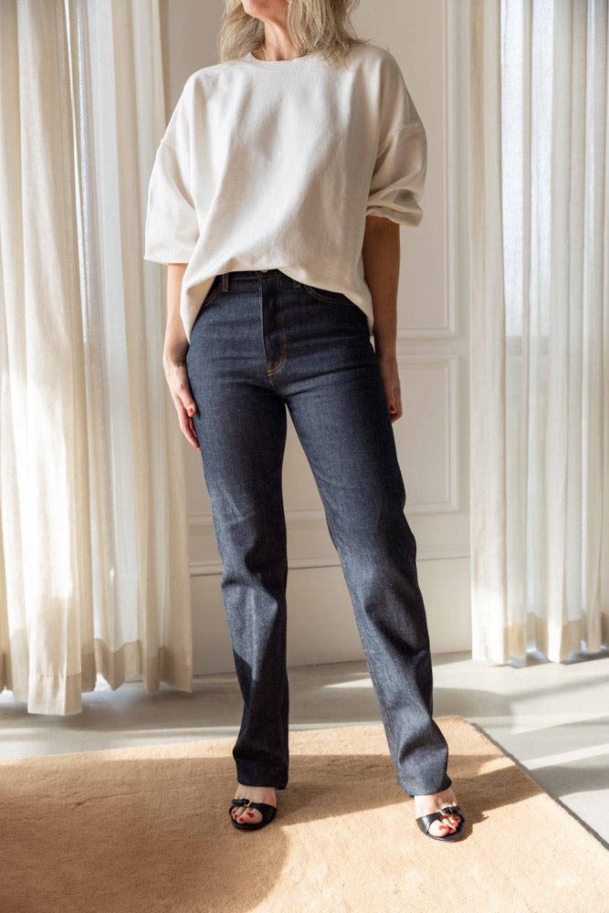 Dagmar Straight Leg Denim in raw blue organic cotton, worn full length with an off-white sweatshirt and black sandals