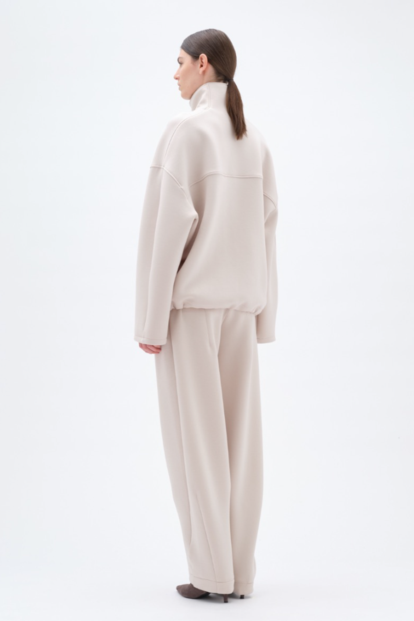 Person wearing a beige soft jacket and matching pants on a white background
