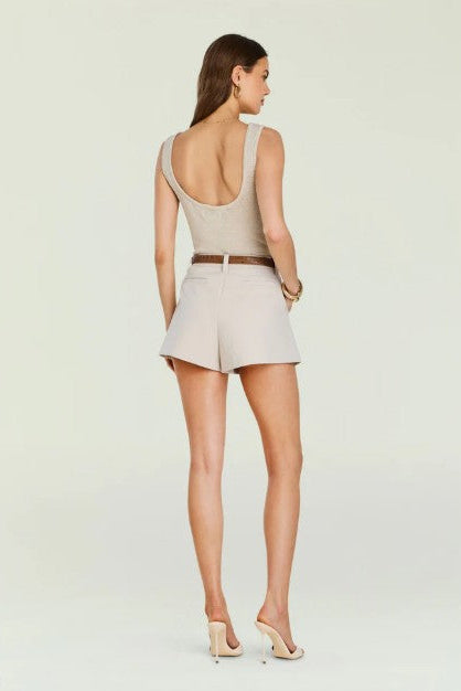 Backside of a woman wearing the seroya hero tank top with pleated shorts in front of a cream background