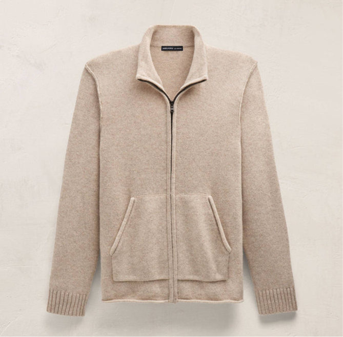 A light beige zip-up knit sweater with a stand collar, front pockets, and ribbed cuffs and hem, displayed against a textured off-white background.