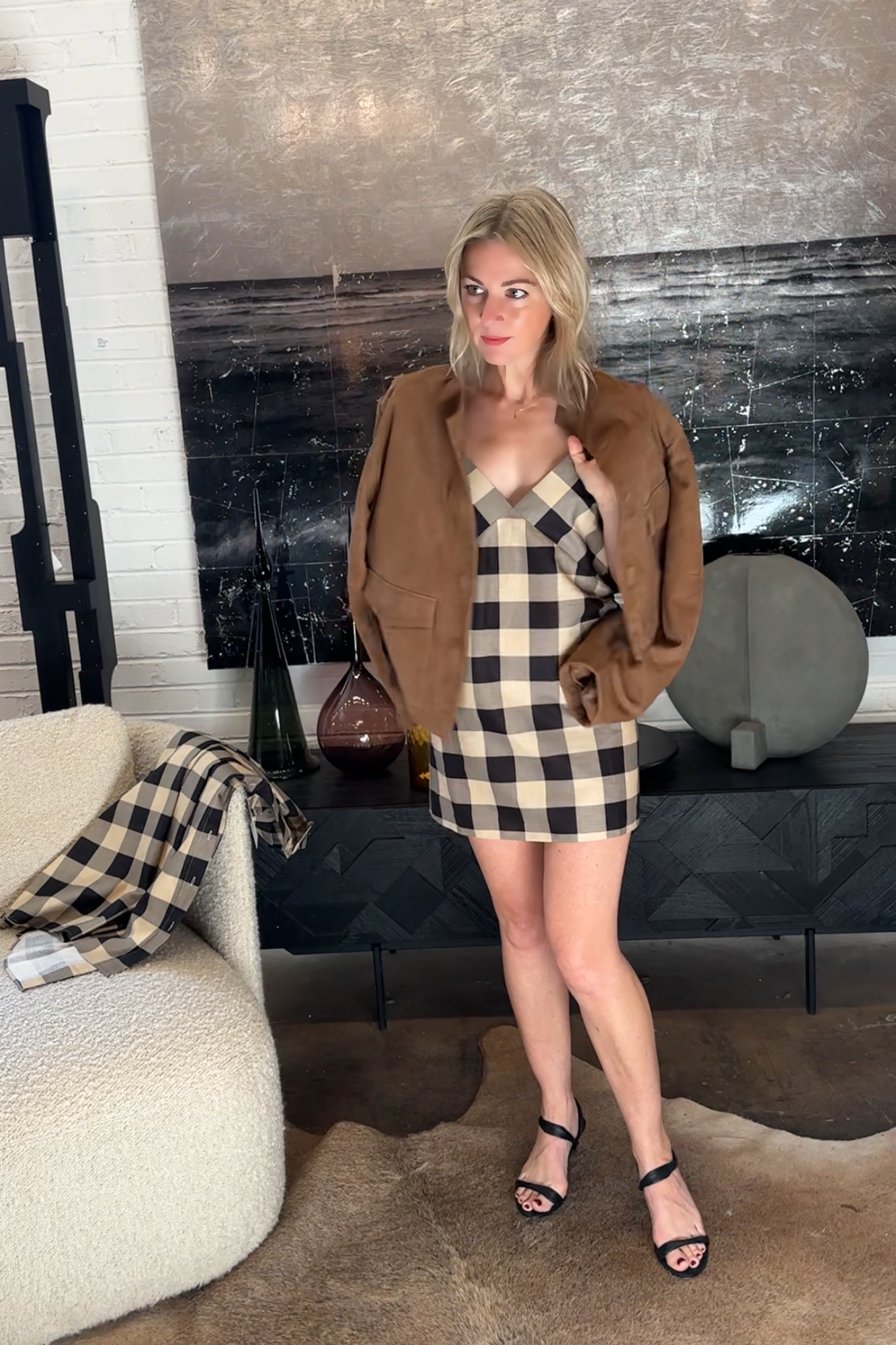 Woman in a plaid dress and brown coat standing in a living room.