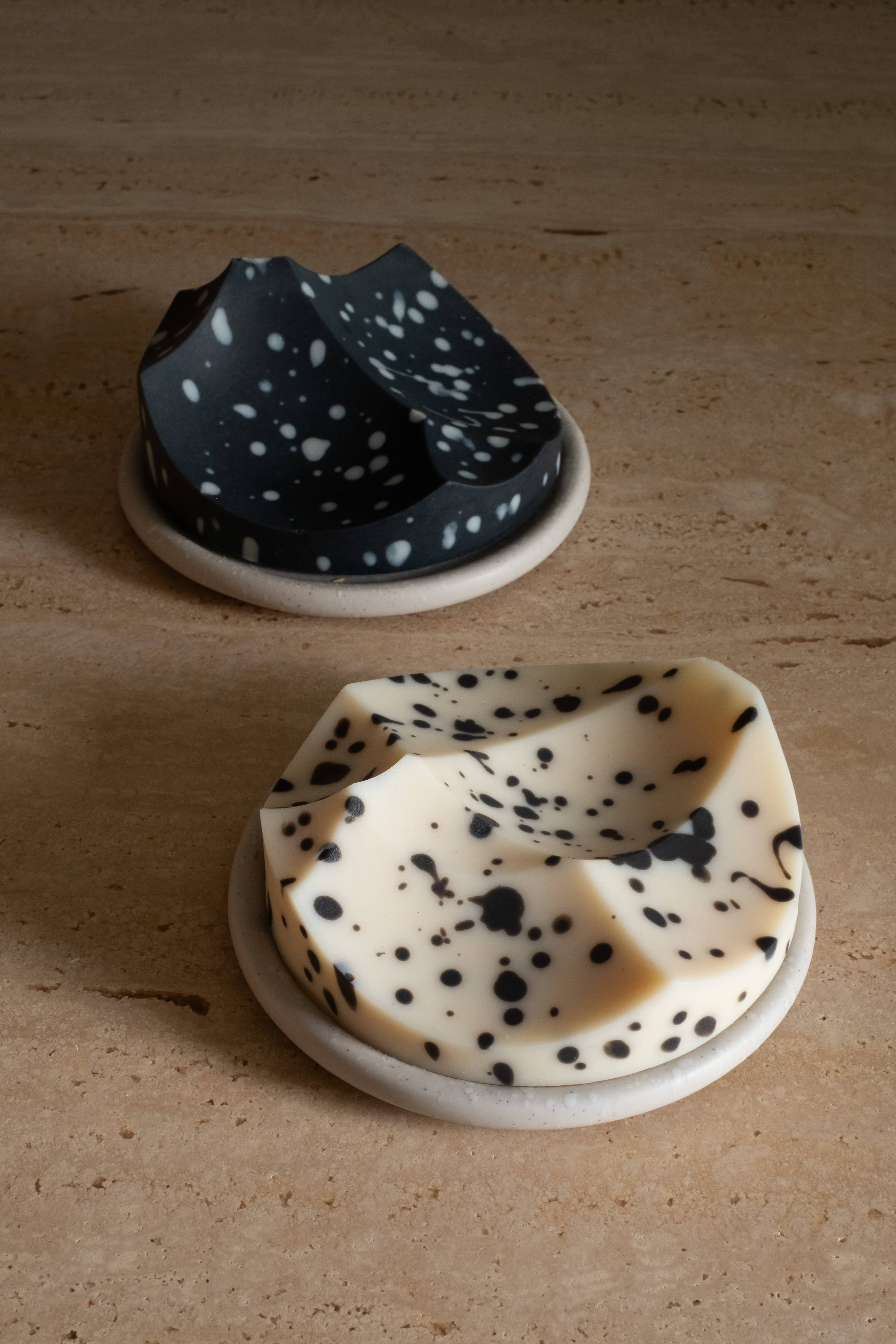 Two ceramic bowls, one black with white spots and one white with black spots, on a wooden surface.