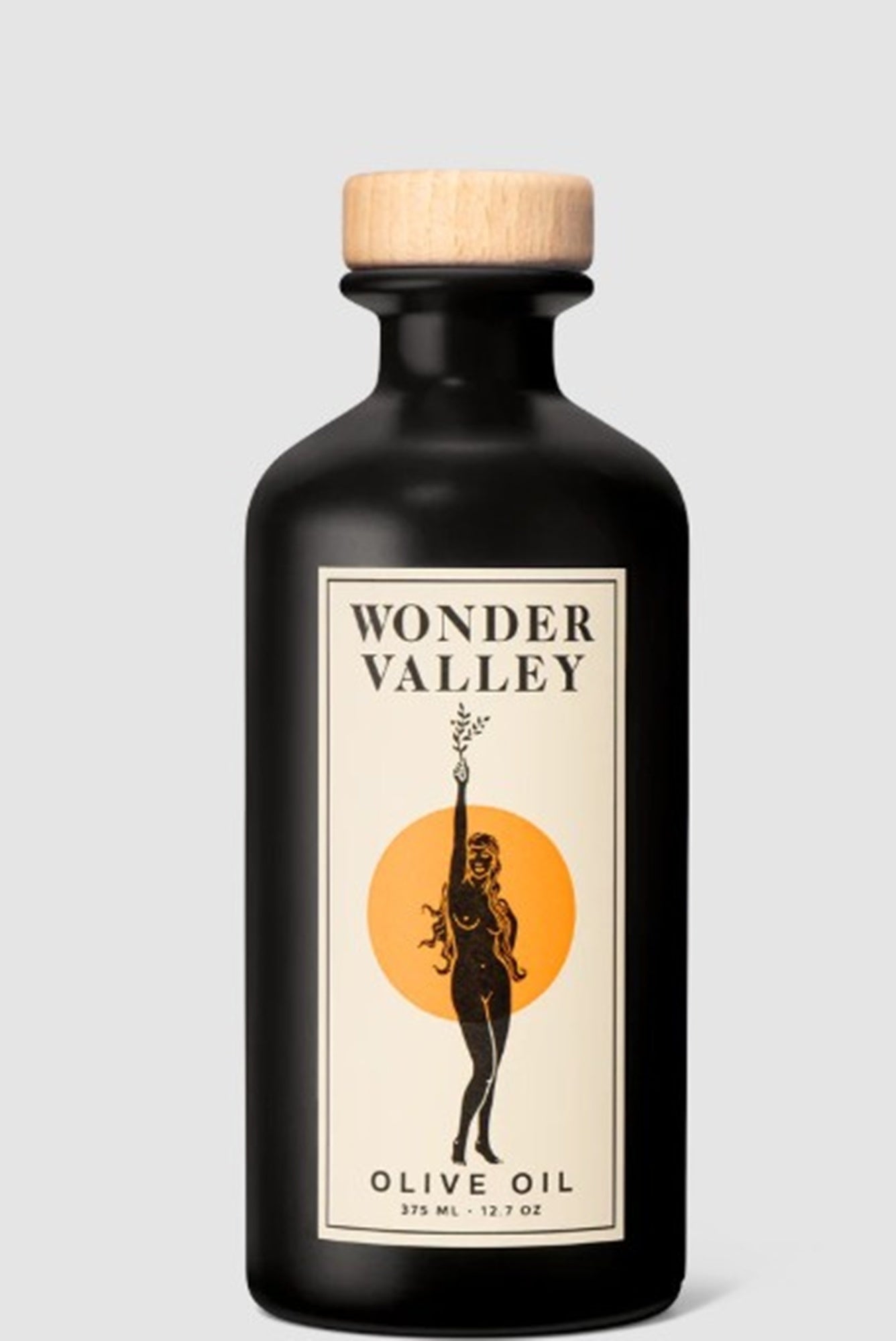 Black olive oil bottle with wooden cap and 'Wonder Valley' label on a light gray background