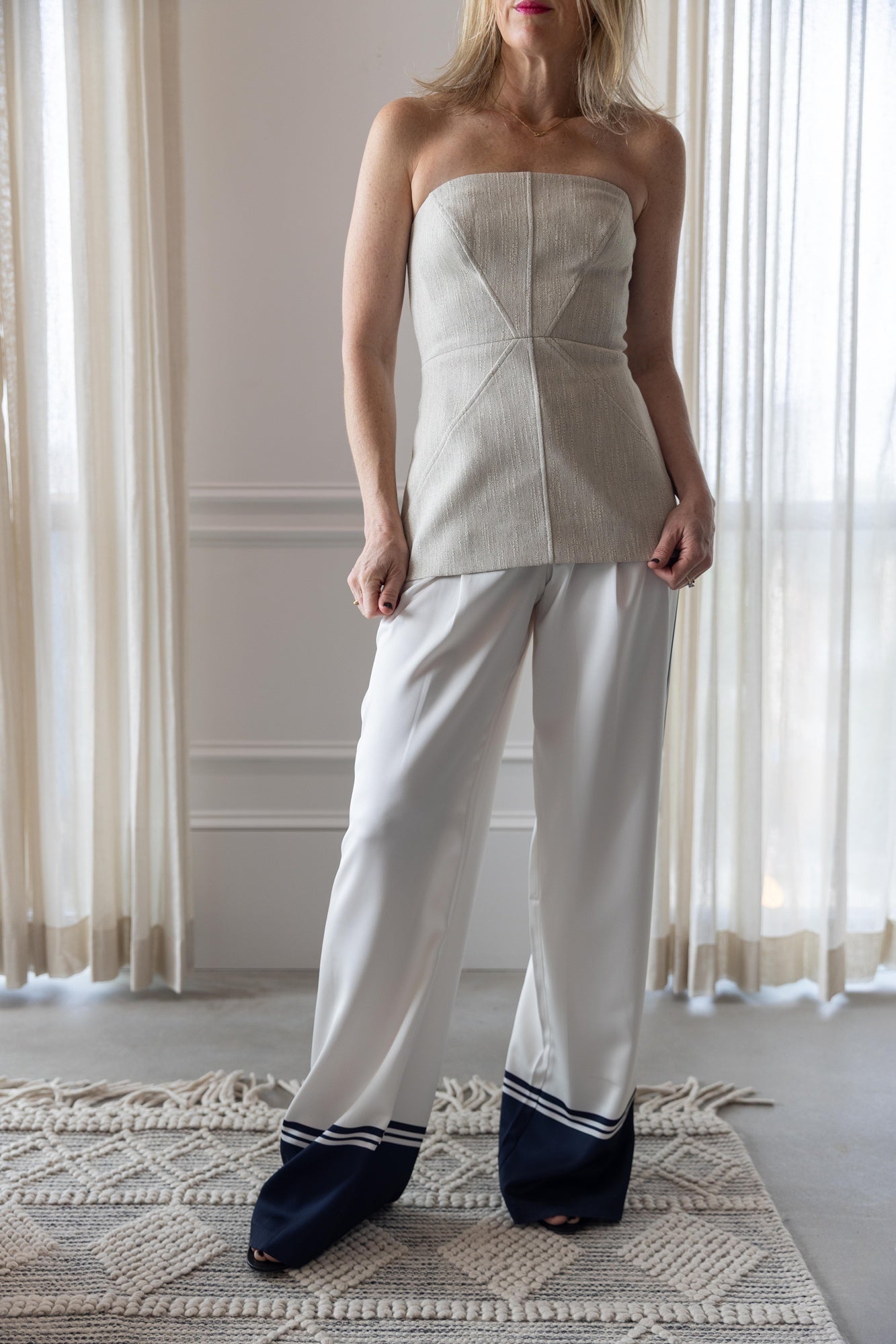 Woman wearing a-emery lovett top and seroya marlowe satin pants standing in a room with tasseled rug and white curtains.