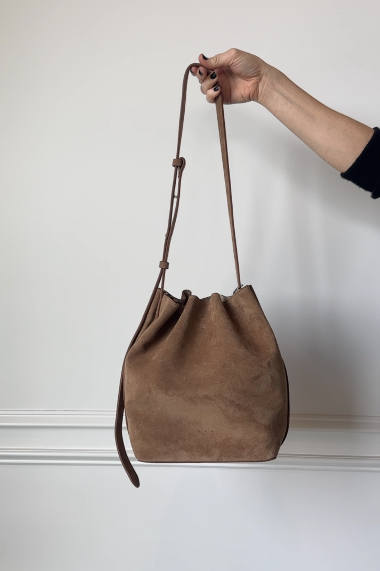 Brown leather bag held by a hand against a plain background