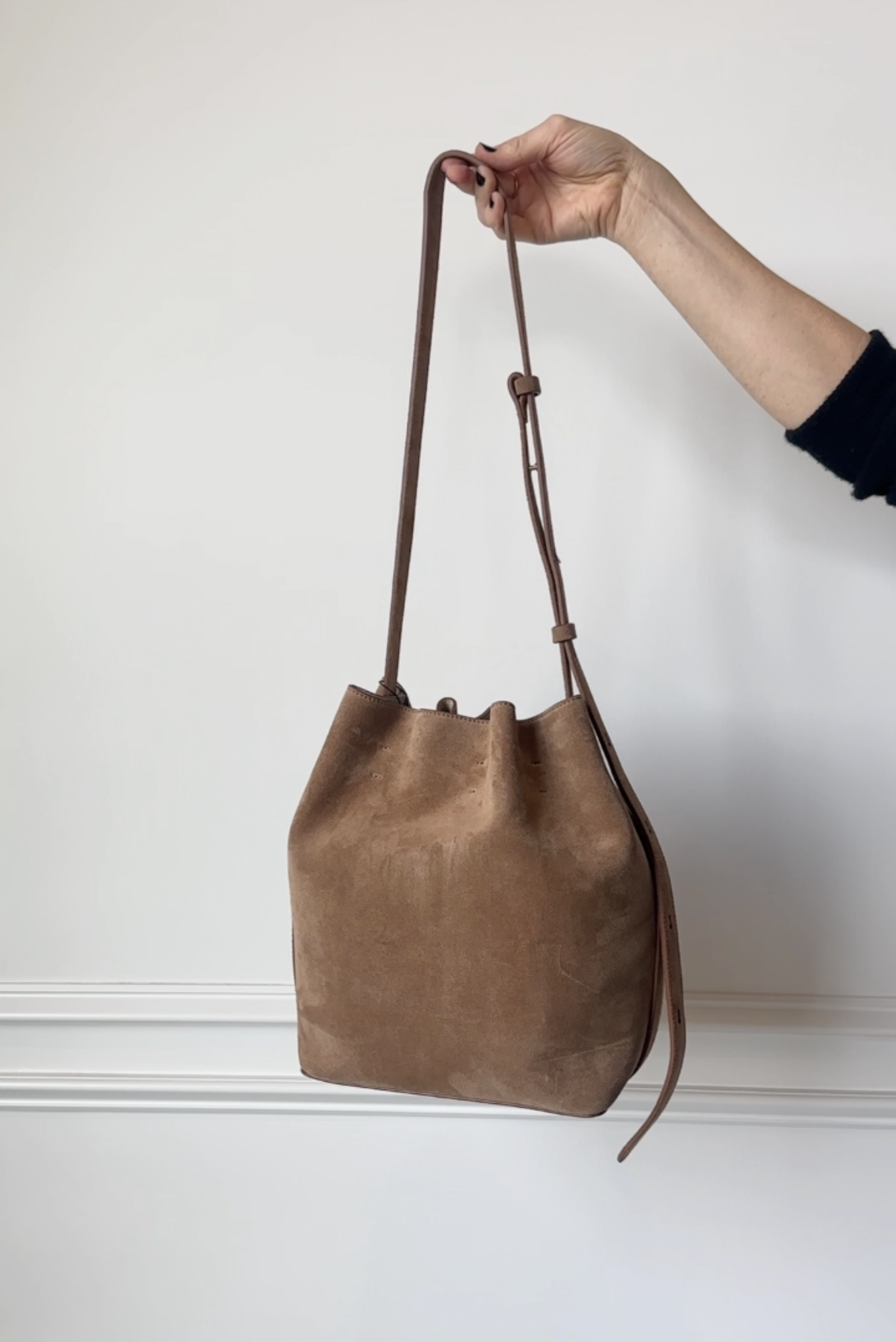 Brown leather handbag held by a hand against a white background