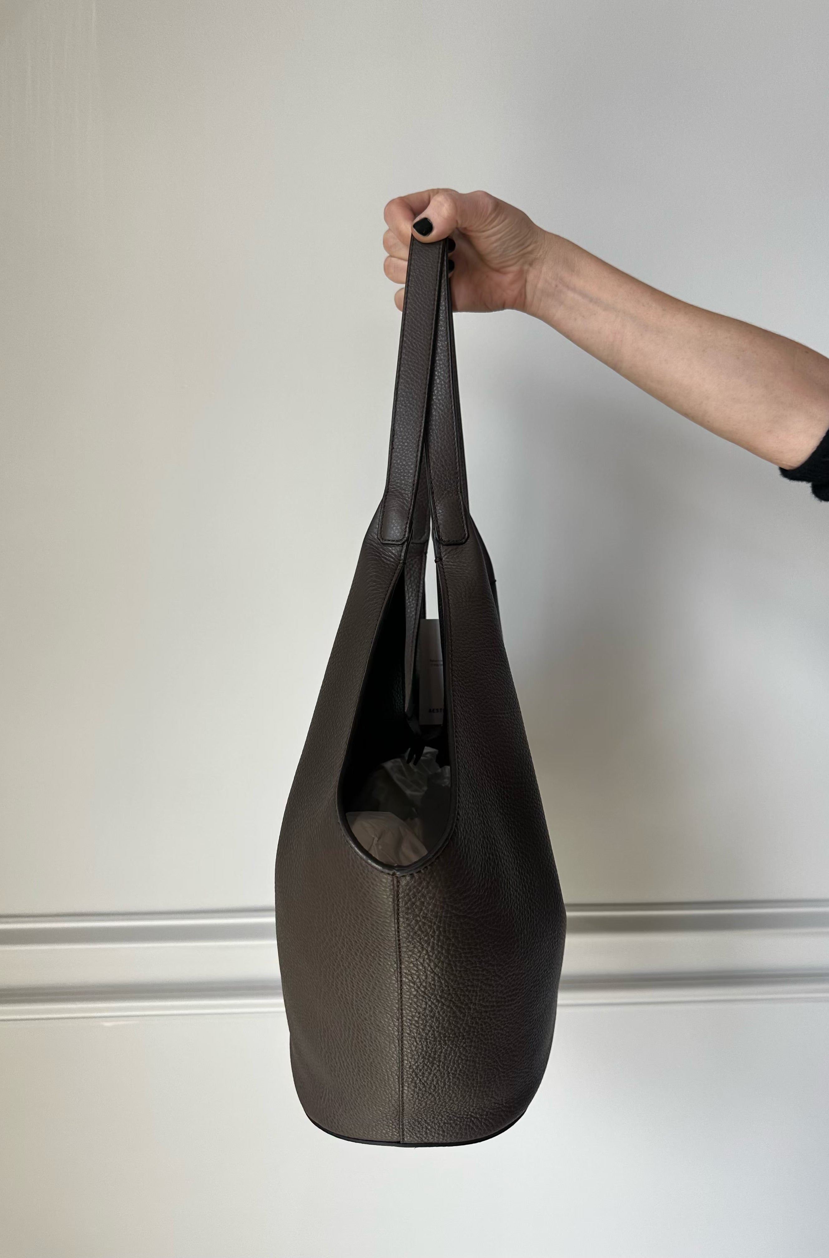Person holding a black leather shoe against a neutral background