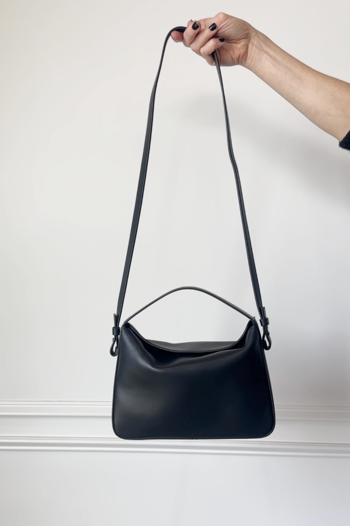 Black handbag held by a hand against a plain background