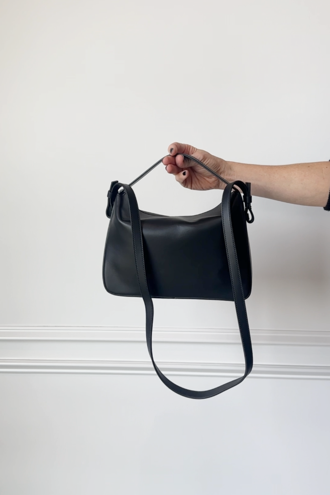 Black handbag held by a hand against a white background