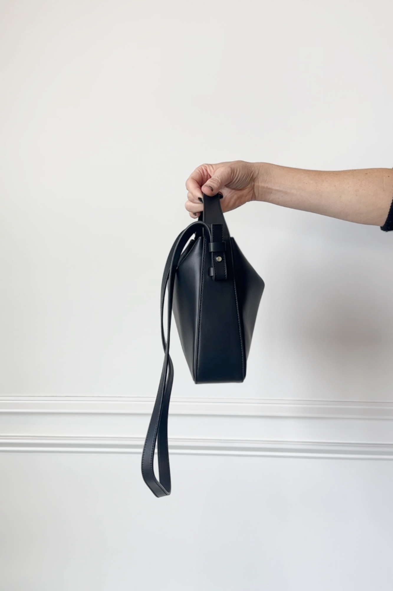 Hand holding a black handbag against a white background