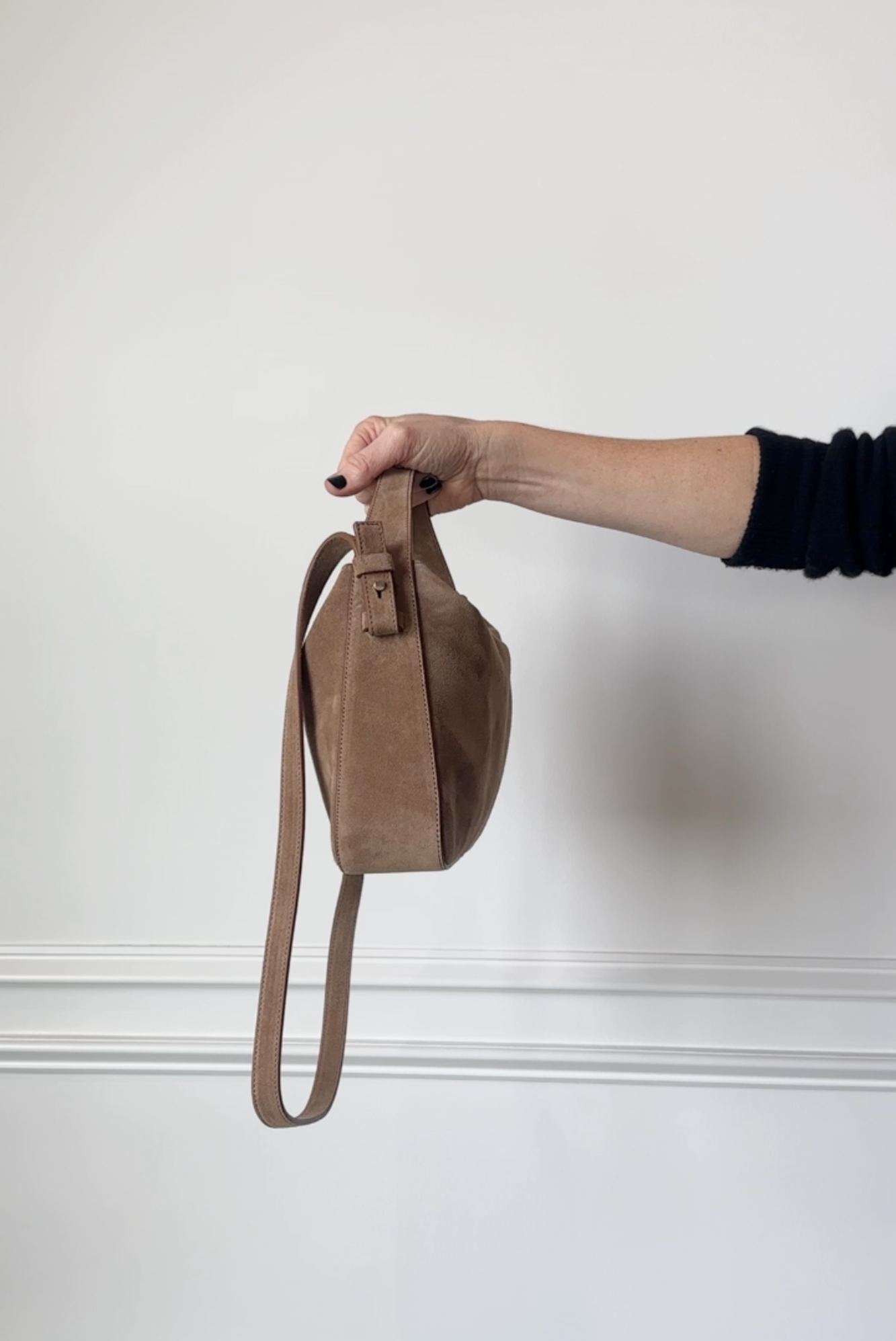 Brown suede handbag held by a person against a white background