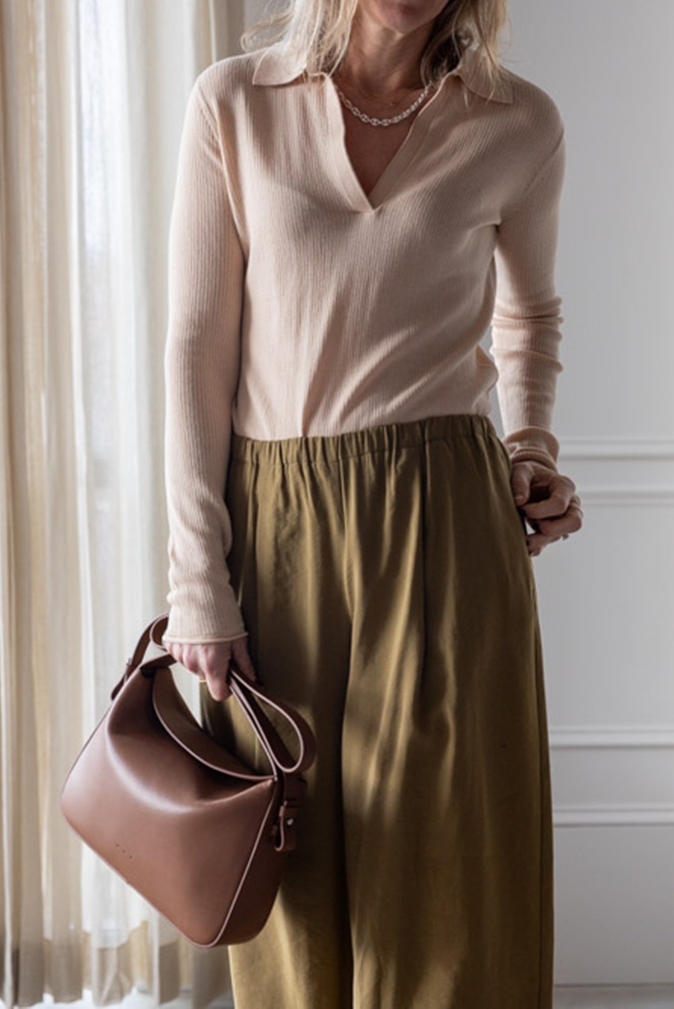 image of a woman wearing the Alysi Maglia Polo and Wide Leg Pull on Trouses with the Aesther Ekme Soft Baguette Bag