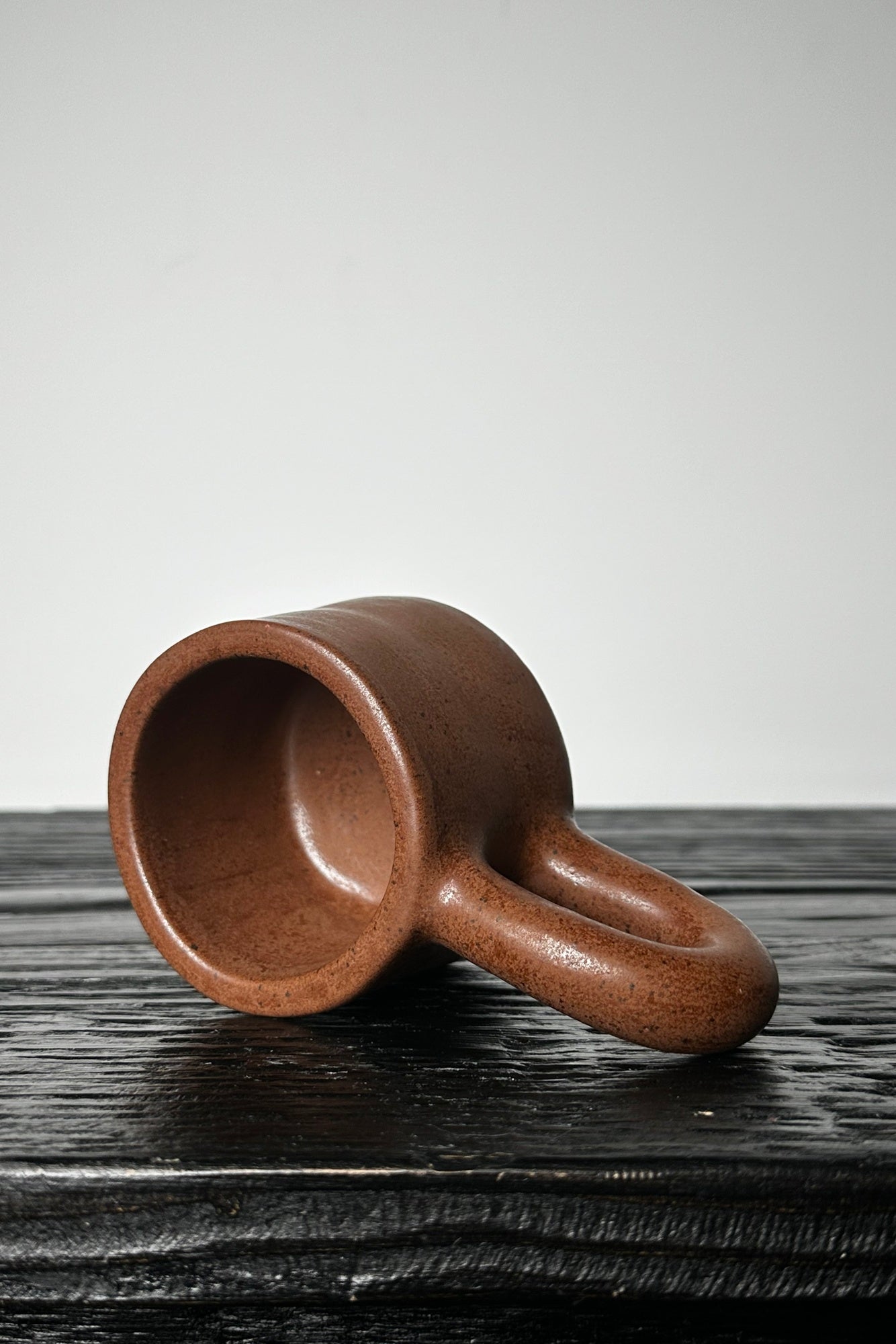 Brown ceramic cup on a dark wooden surface with a light gray background