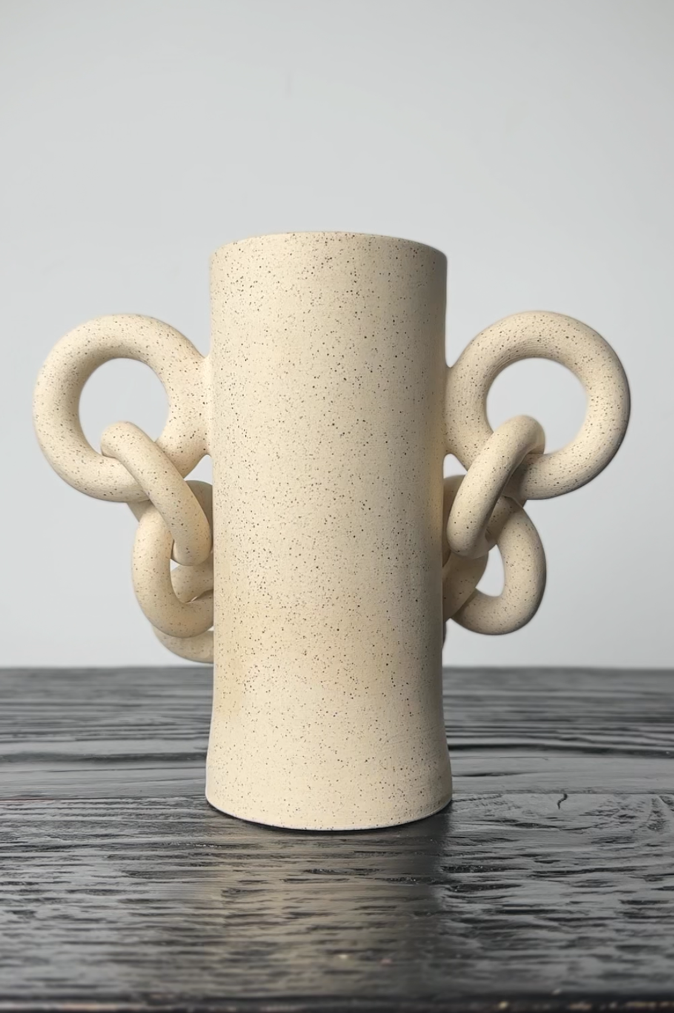 Beige ceramic vase with unique handles on a wooden surface