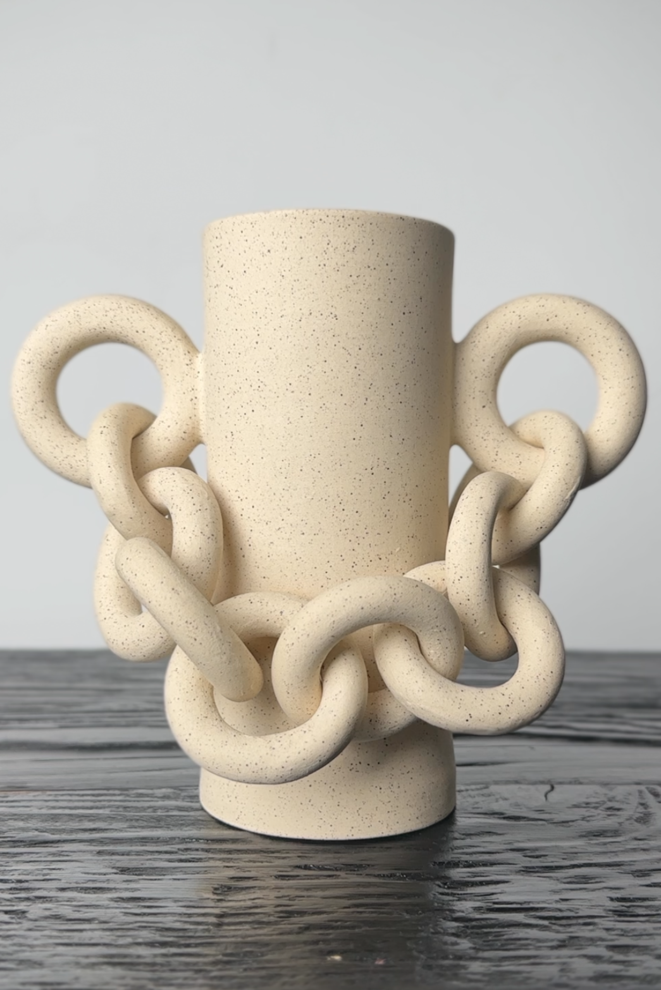Beige ceramic vase with chain-like design on a gray surface