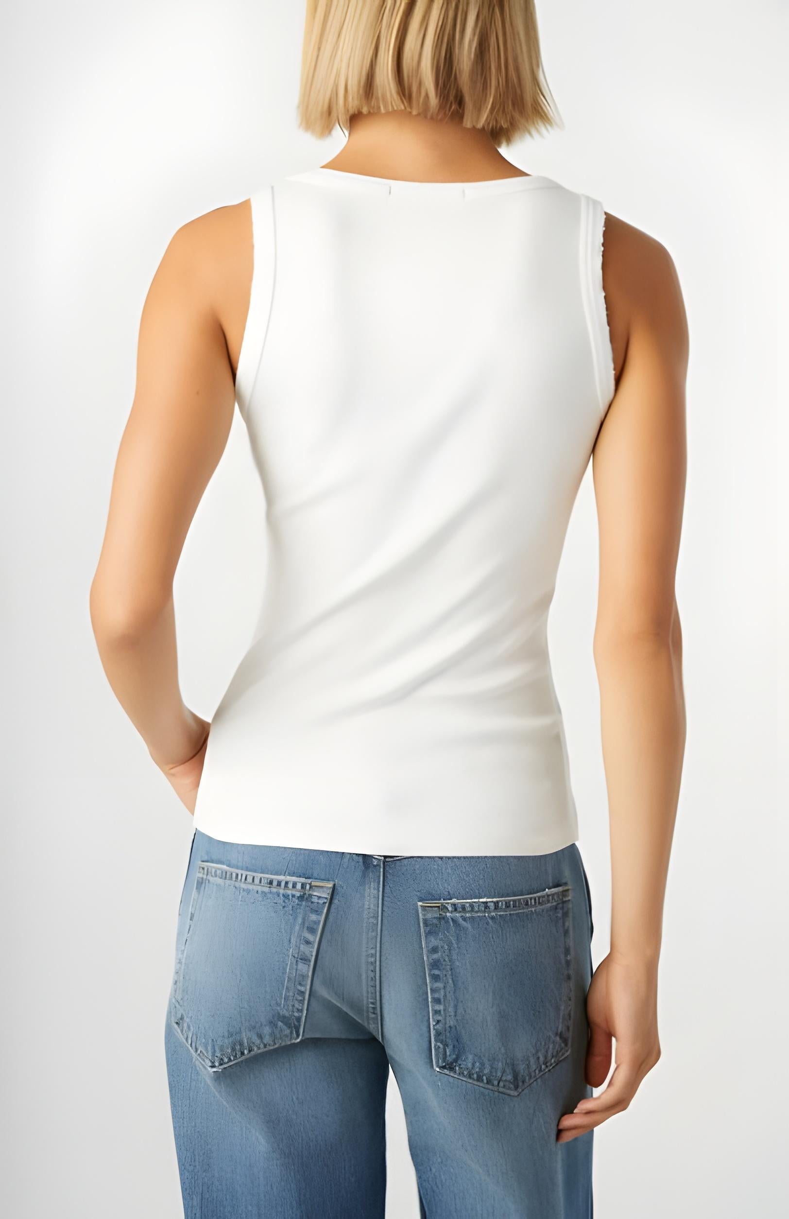 Person wearing a white sleeveless top and blue jeans on a plain background