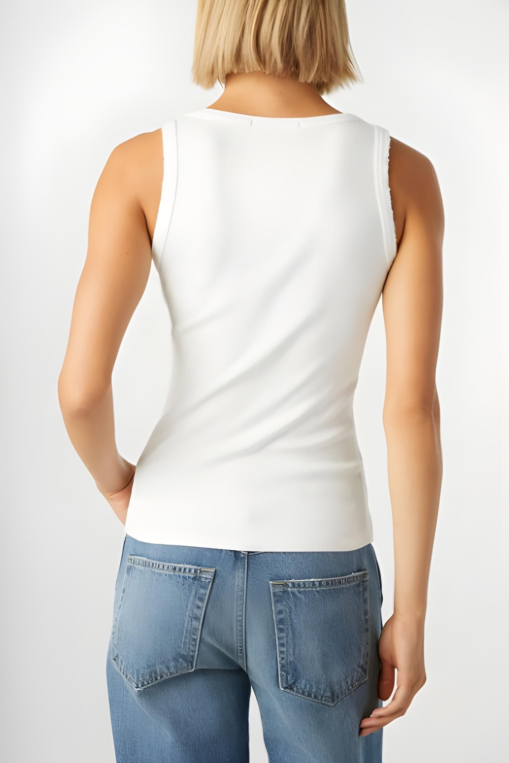 Person wearing a white sleeveless top and blue jeans on a plain background