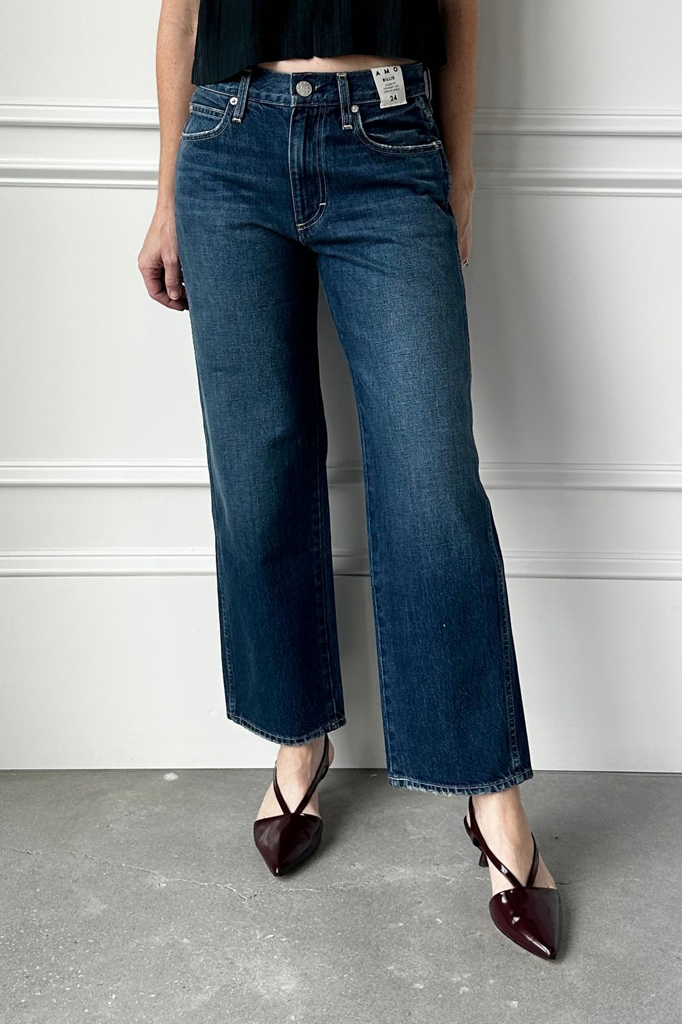 Person wearing blue jeans and black shoes against a white wall.