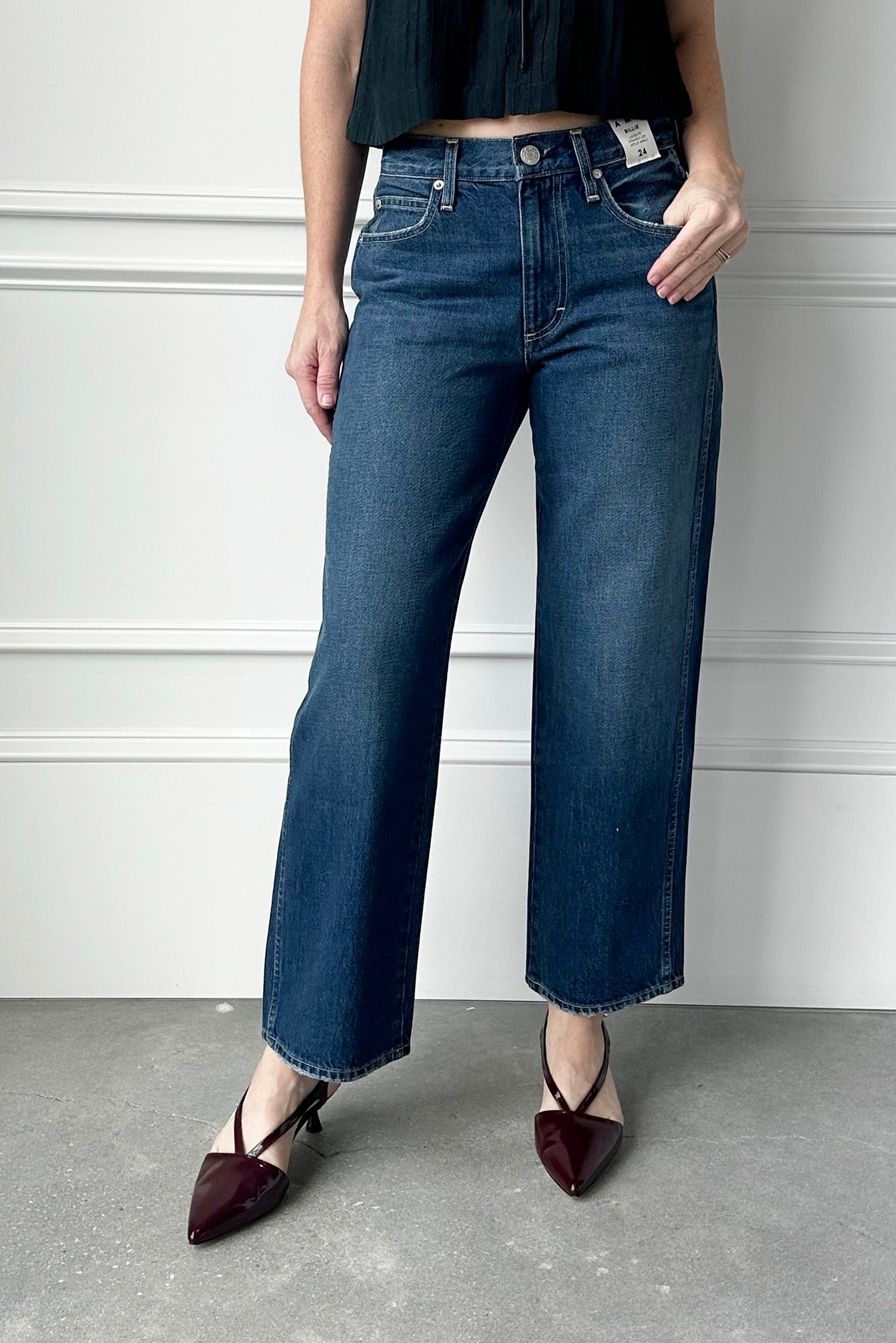 Person wearing blue jeans and black shoes against a white wall.