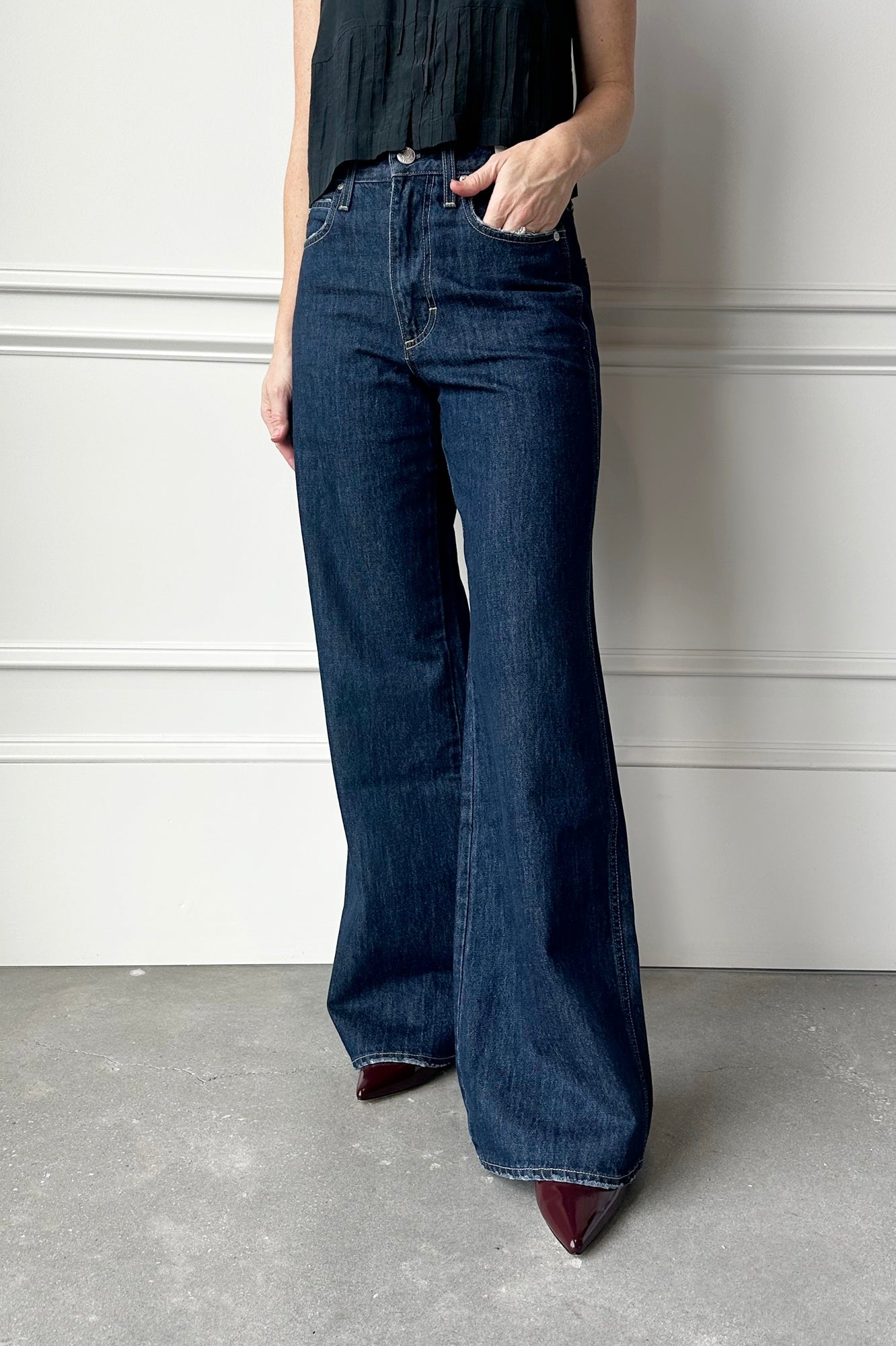 Person wearing blue flared jeans against a white wall.