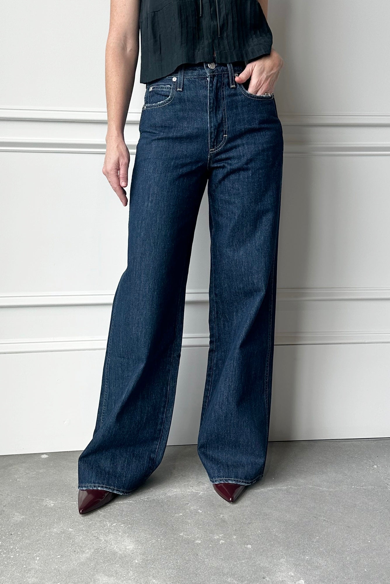 Person wearing dark blue wide-leg jeans against a white wall.