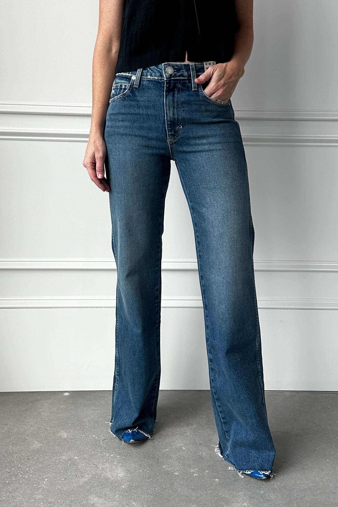 Person wearing blue jeans standing against a white wall.