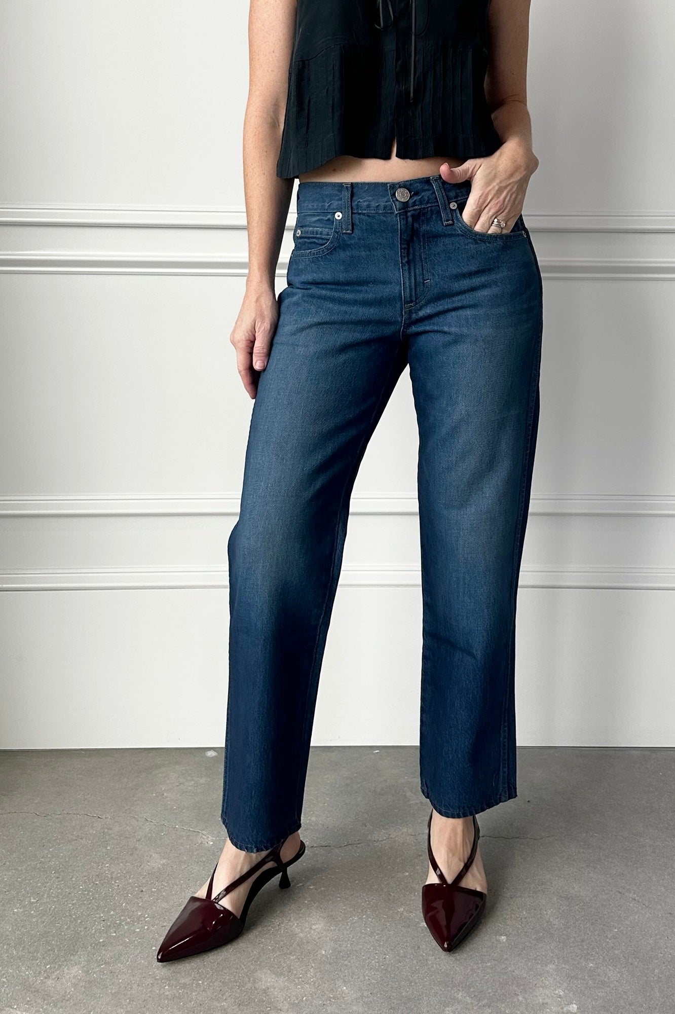 Person wearing dark blue jeans and black top against a white wall.