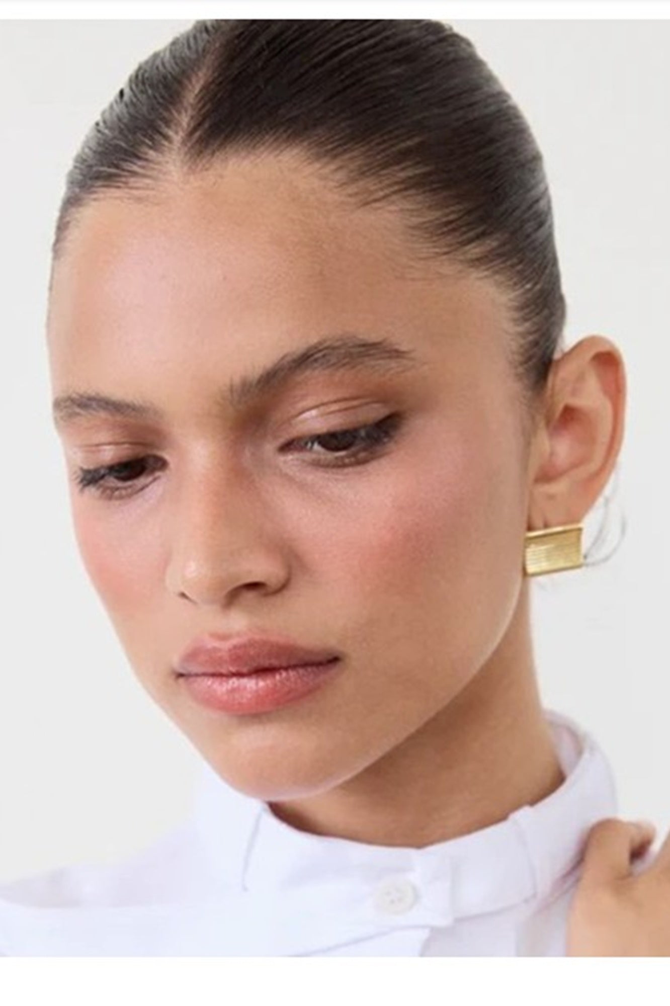 Close-up of a person wearing a white shirt with a gold earring on a plain background