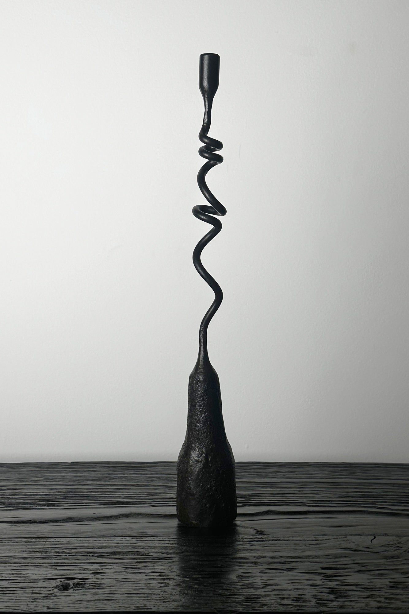 Black spiral sculpture on a wooden surface with a white background