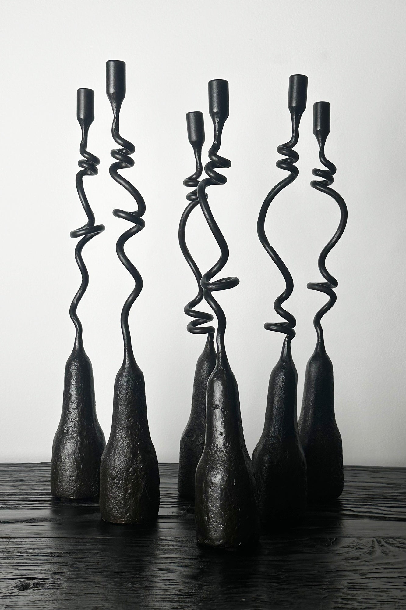 Set of five twisted metal candle holders on a wooden surface with a white background