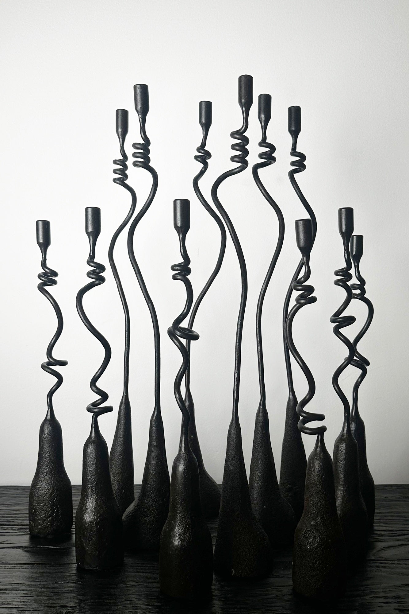Set of black metal candle holders with twisted designs on a wooden surface.
