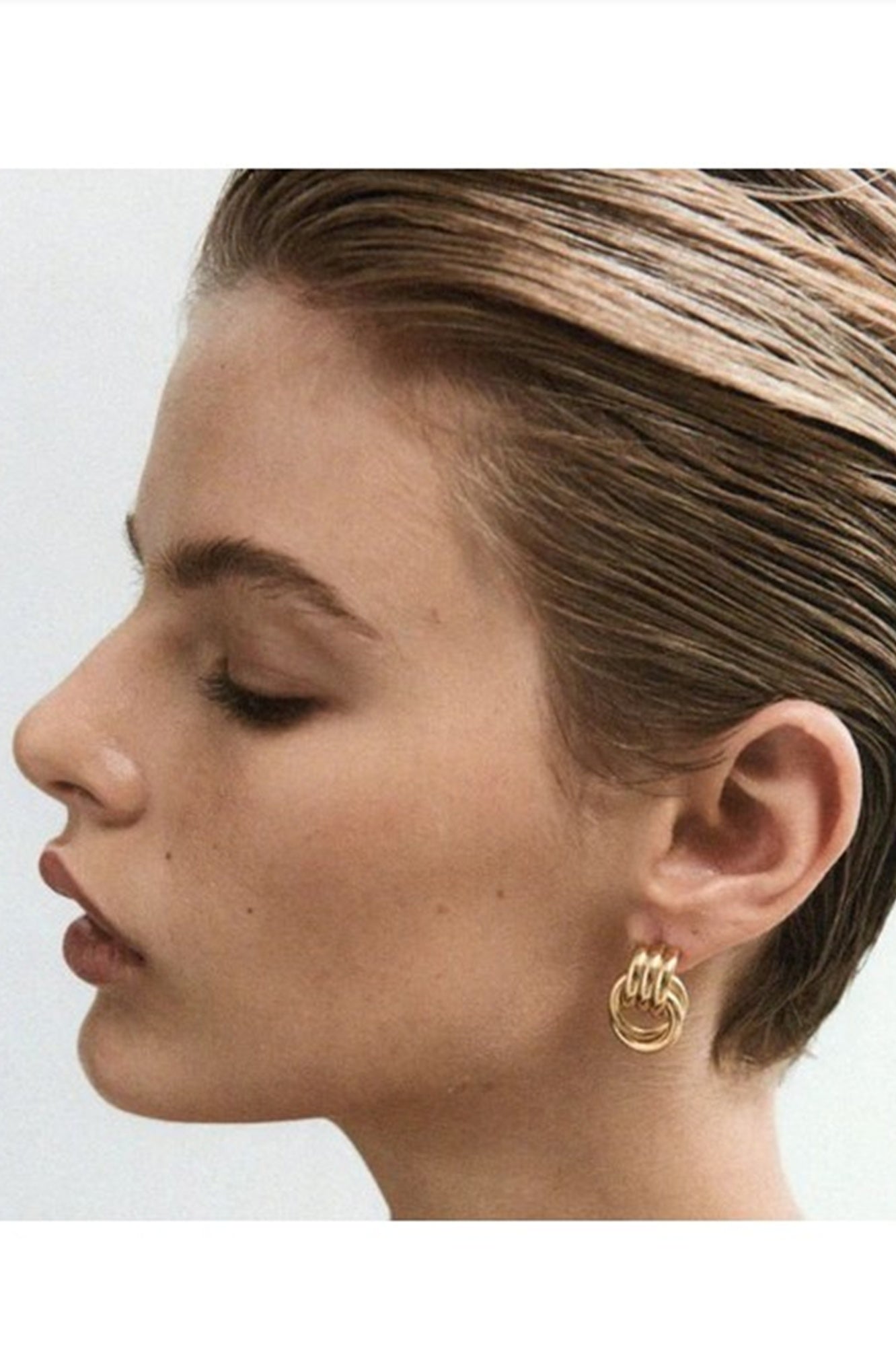 Close-up of a person wearing gold hoop earrings on a white background