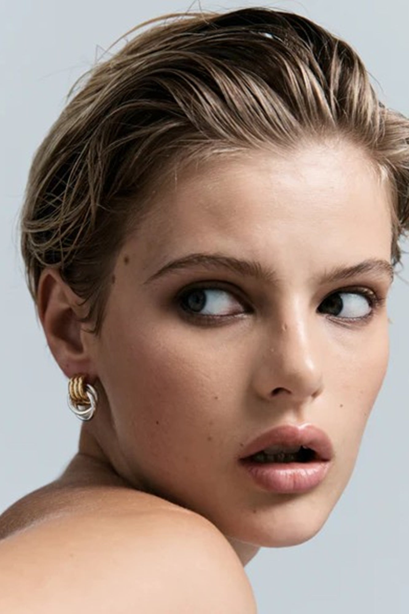 Close-up of a woman with styled hair and earrings against a light background