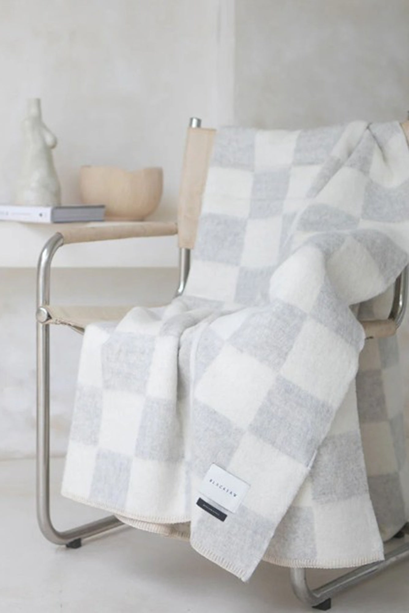 Gray and white checkered blanket draped over a chair in a minimalistic setting