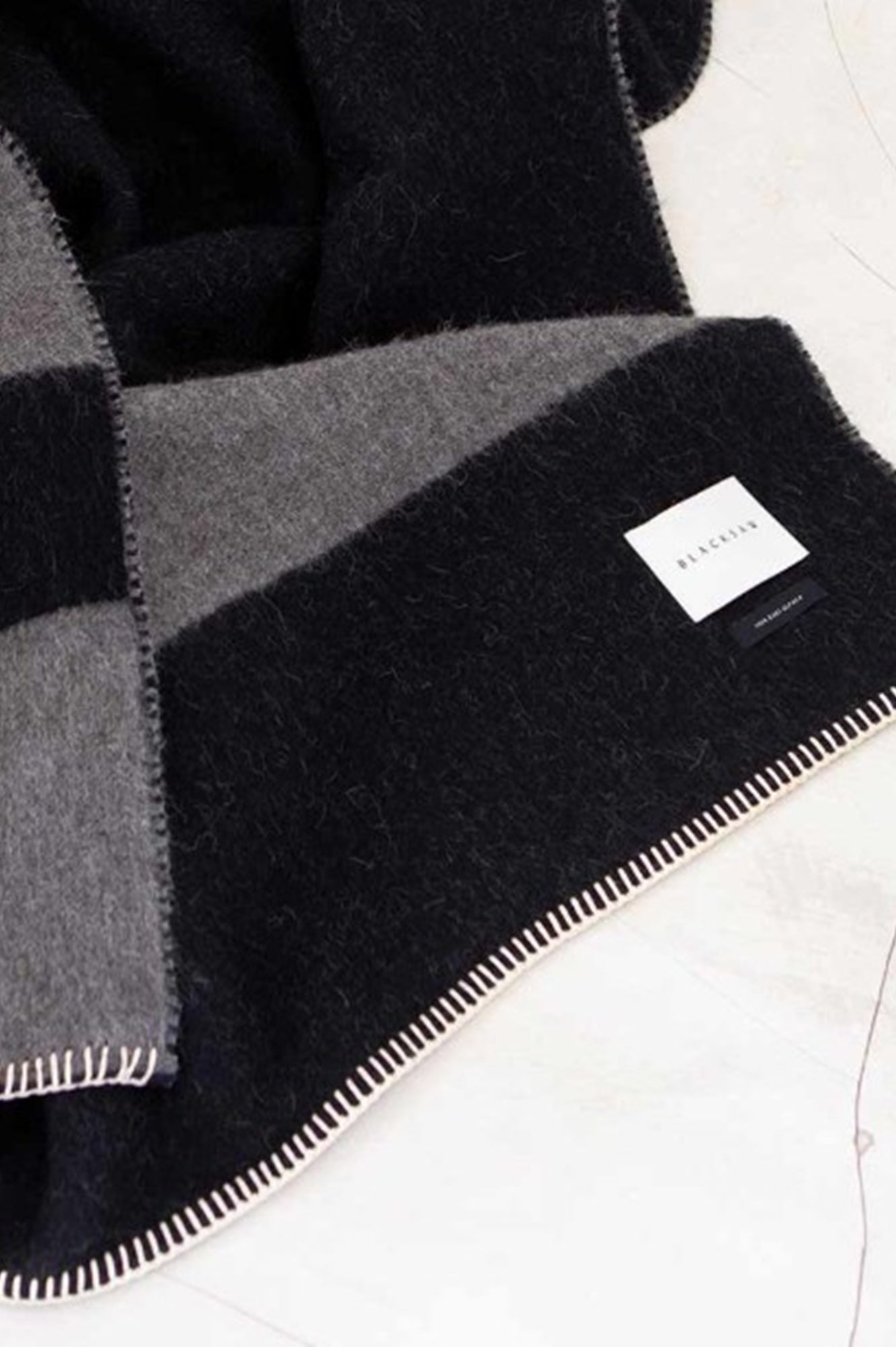 Black, gray, and white checkered blanket with a brand label on a white background