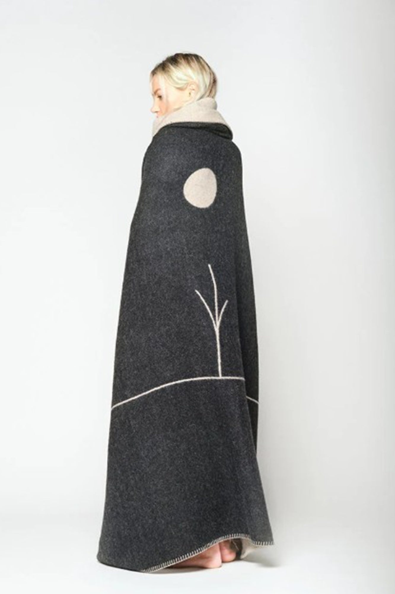 Person wrapped in a dark gray blanket with a circular cutout on a white background