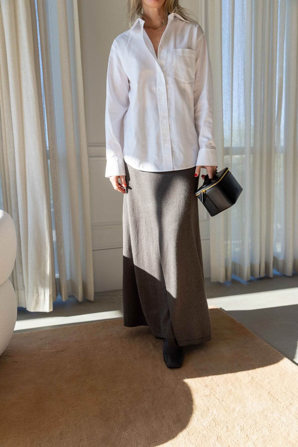 by Malene Birger Audrey Top in white, full-length look with a grey maxi skirt and black vanity bag in a sunlit room
