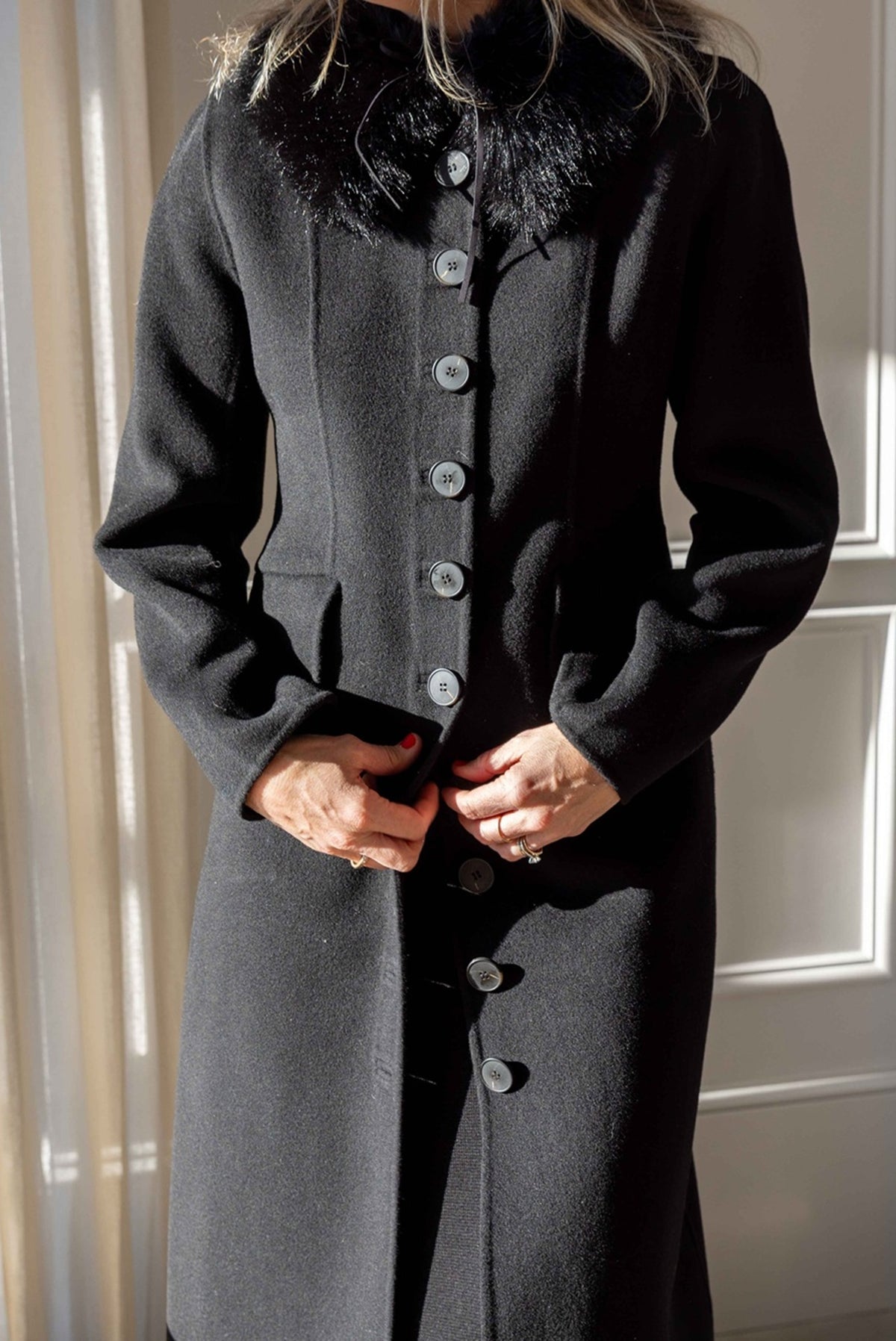 Close-up of the by Malene Birger Magdalena Coat in black wool with button front, worn with the black Cowie Faux Fur Scarf at the collar