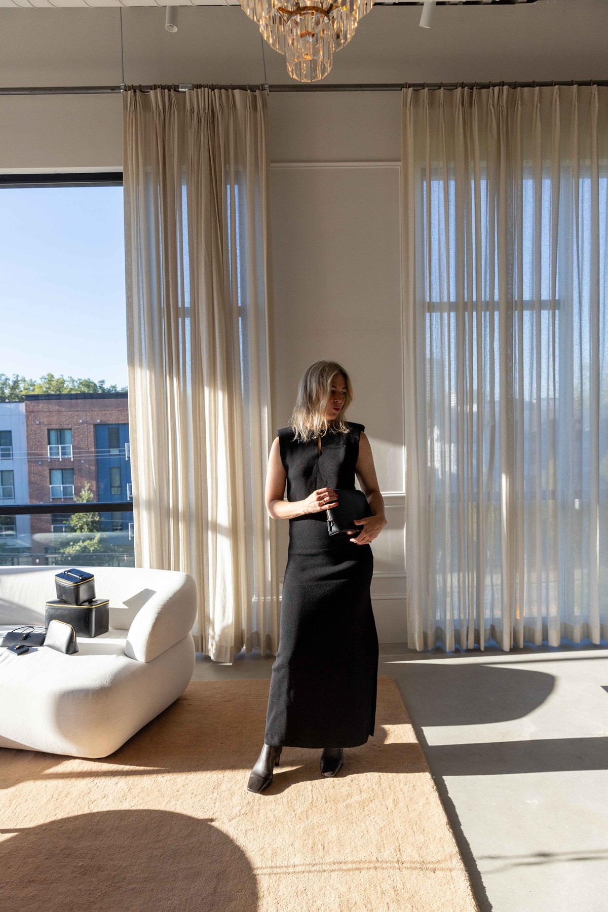 by Malene Birger Rowen Dress in black, sleeveless midi worn with boots, full-length view in a bright loft