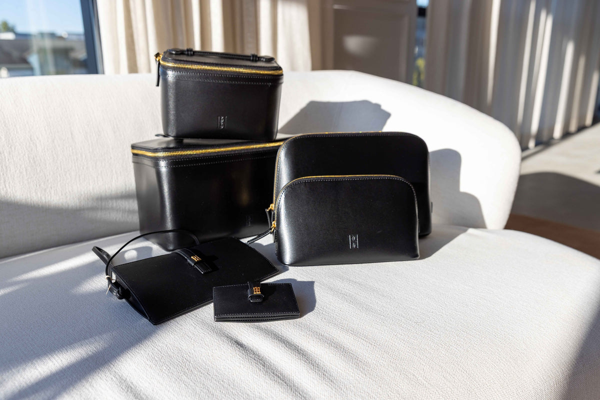 by Malene Birger Vera and Aya black leather accessories collection: wallet, phone case, beauty bags and cosmetics cases arranged on a white sofa