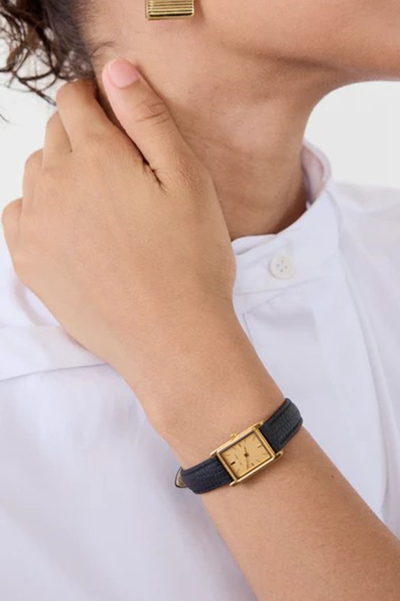 Person wearing a gold watch with a black strap on a white background