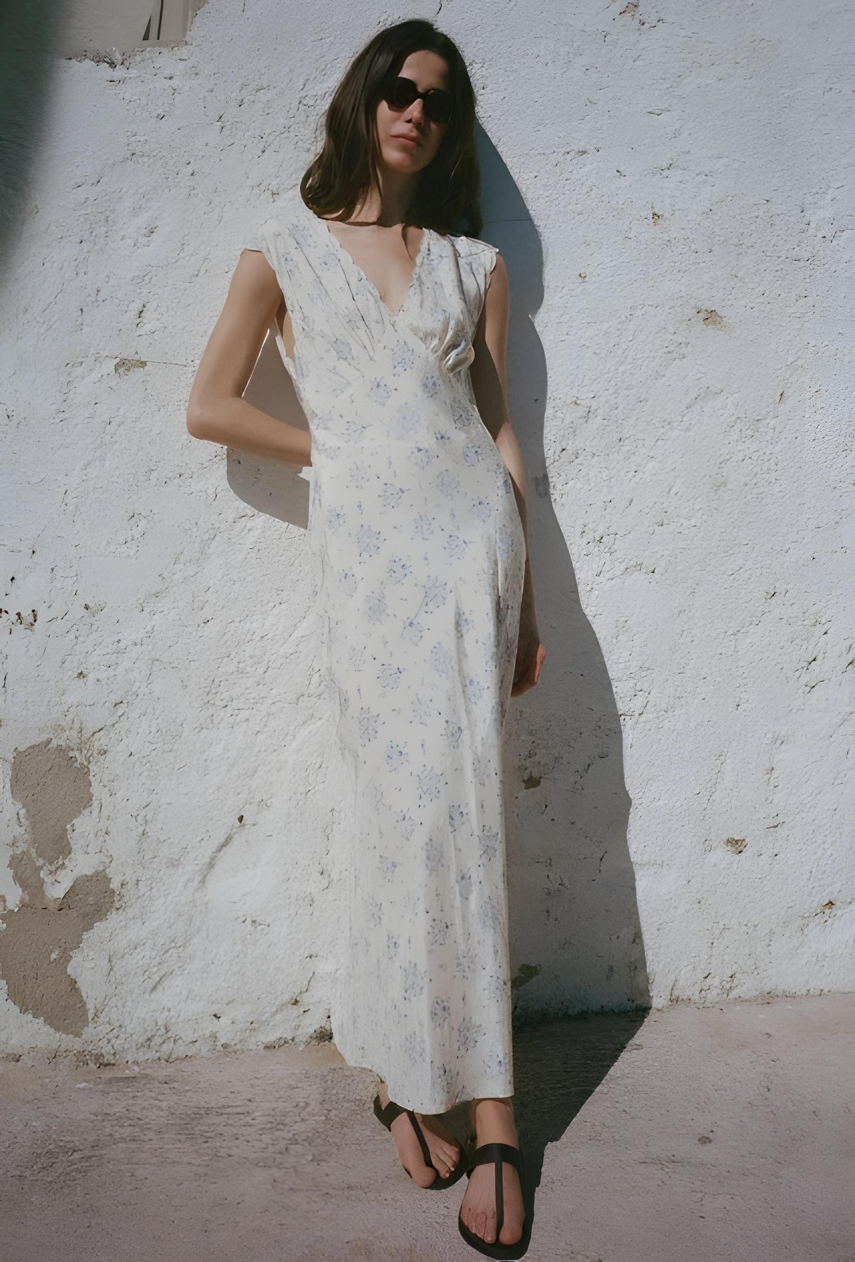 Woman in a white floral dress standing against a textured white wall.