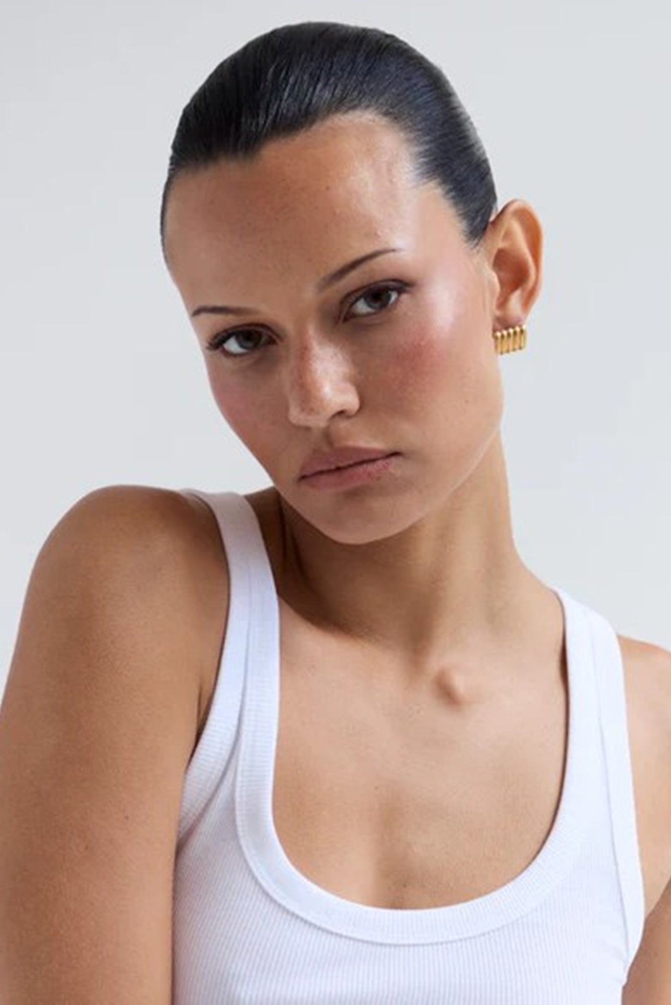 Woman wearing a white tank top against a plain background