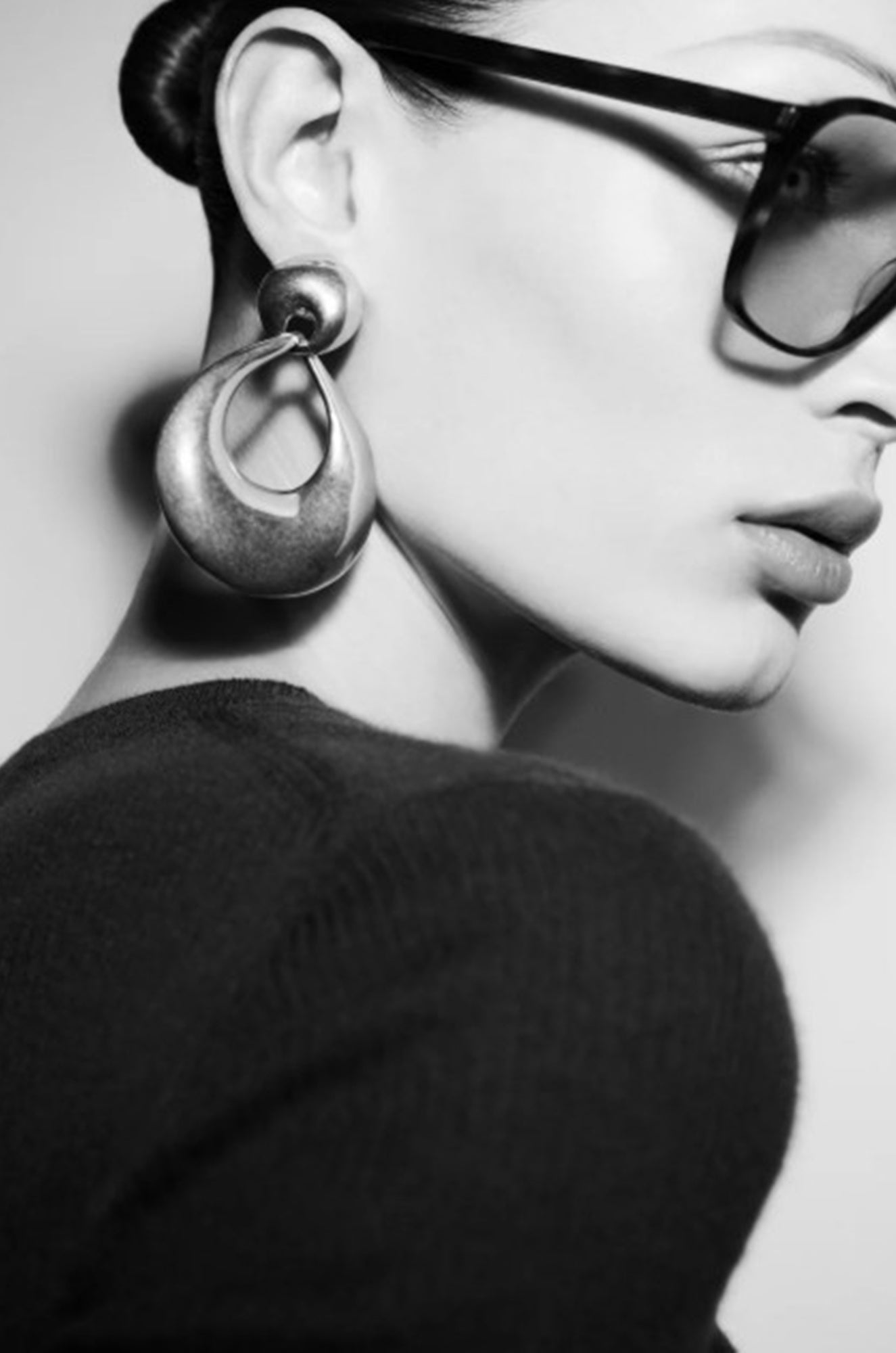 Close-up of a person wearing large hoop earrings and sunglasses with a blurred background