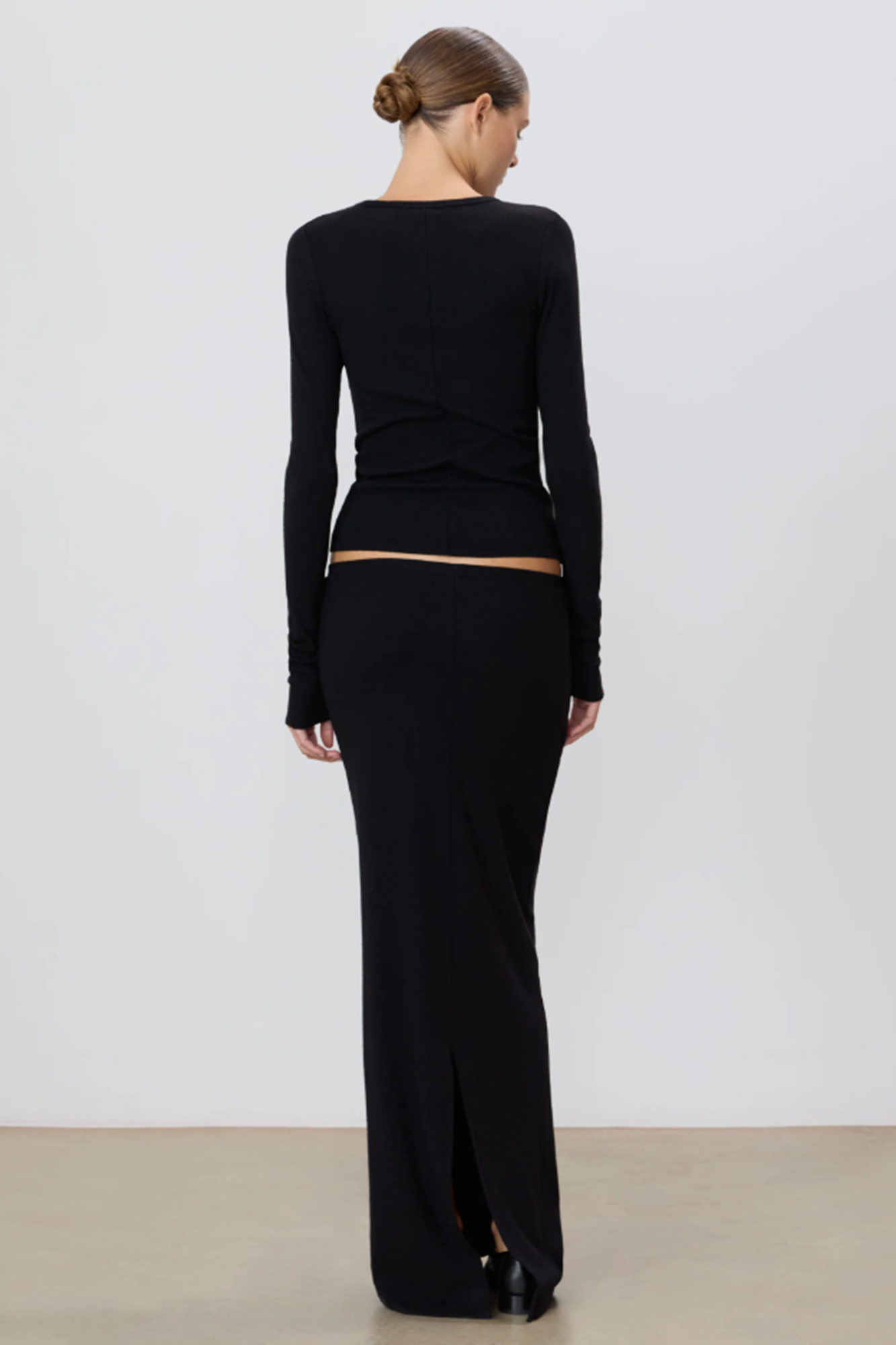 Woman wearing a black long-sleeve top and black skirt against a white background