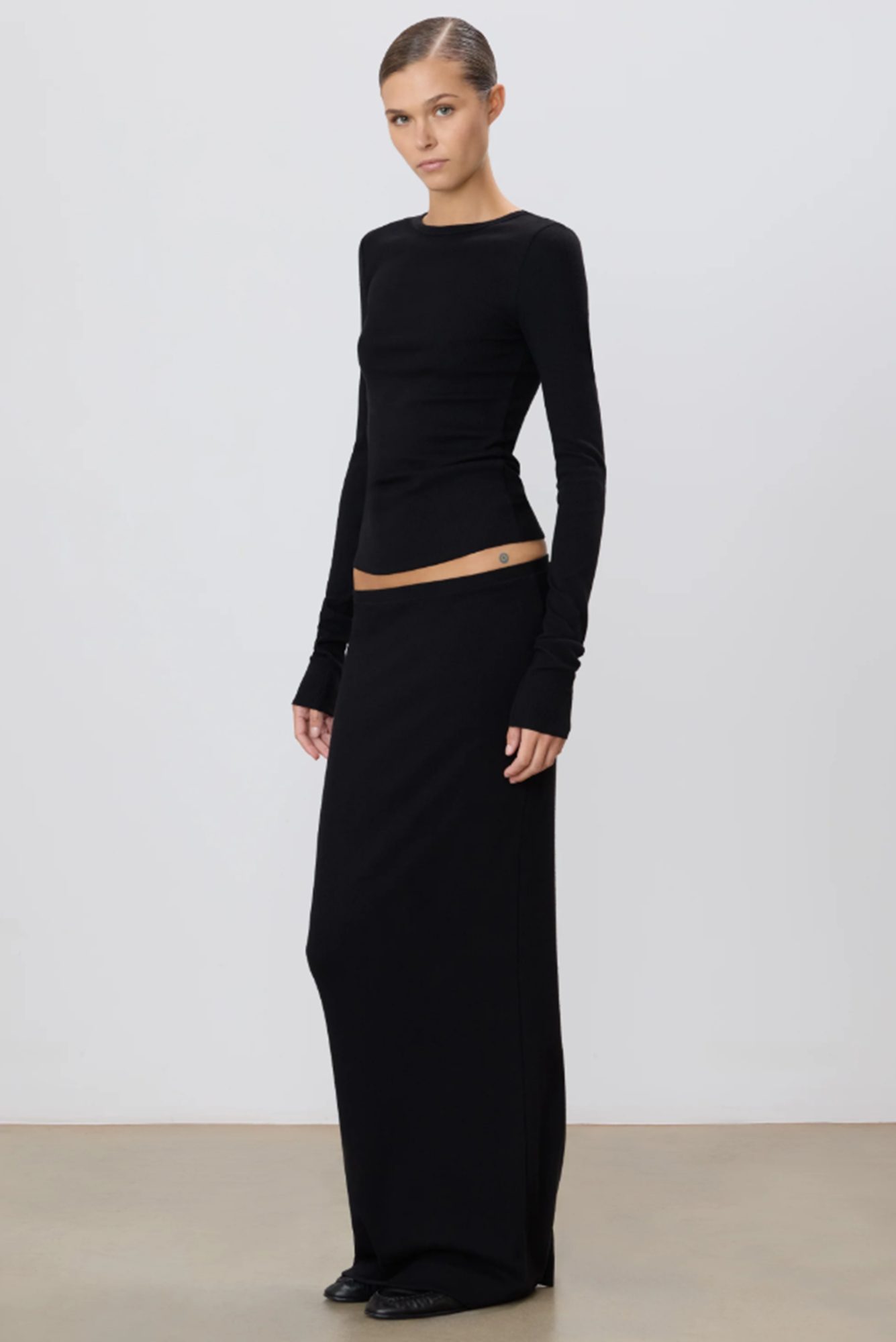 Woman wearing a black long-sleeve top and black skirt against a white background